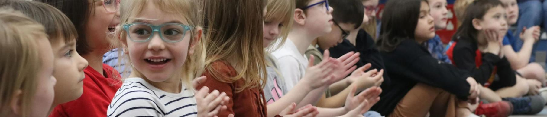 Elementary students smiling and clapping together in a classroom