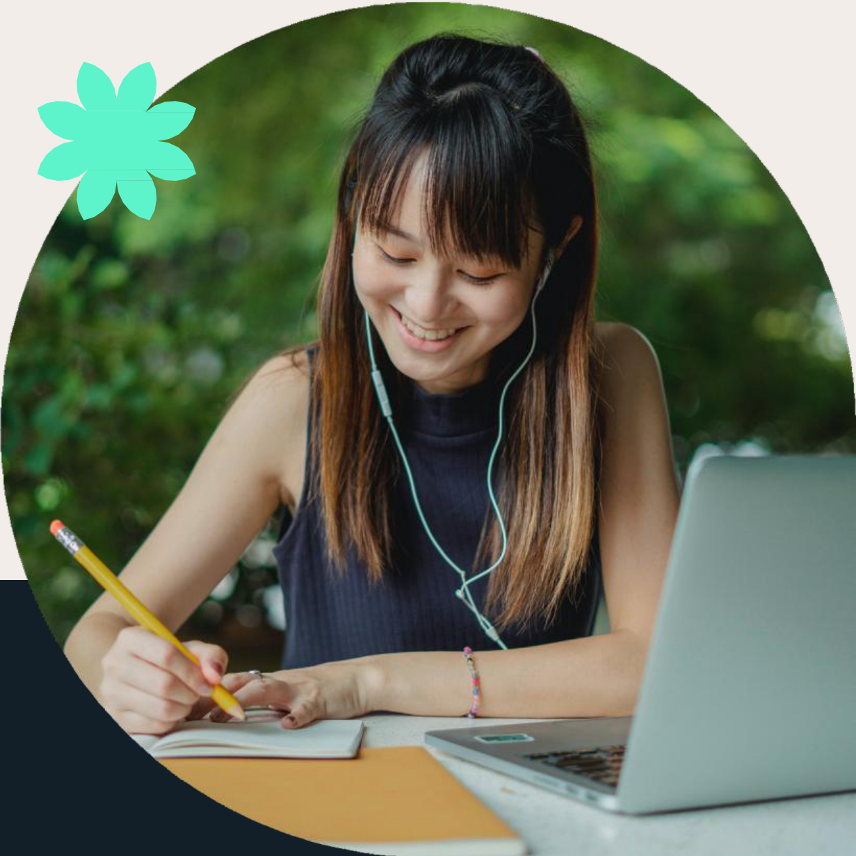 Smiling person wearing headphones, writing notes and using a laptop