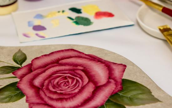 A detailed painting of a red rose on a ceramic tile or palette