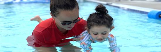 Swim instructor teaching a young child how to float in the pool.