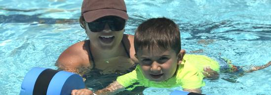 A young child in a neon yellow shirt practicing swimming with a private instructor in an outdoor pool.