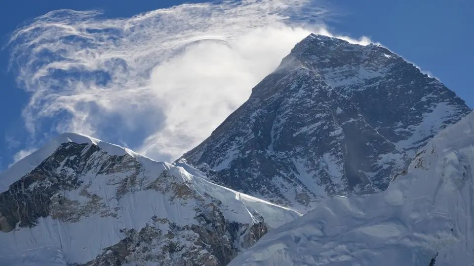 Snow-covered mountain peak rising through swirling clouds under a blue sky
