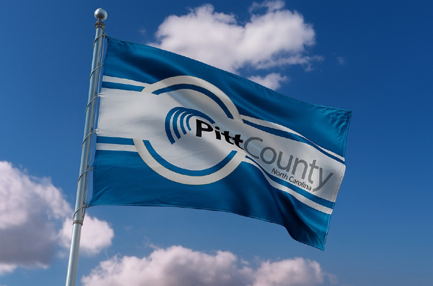 Pitt County North Carolina flag flying on a flagpole against a blue sky with clouds