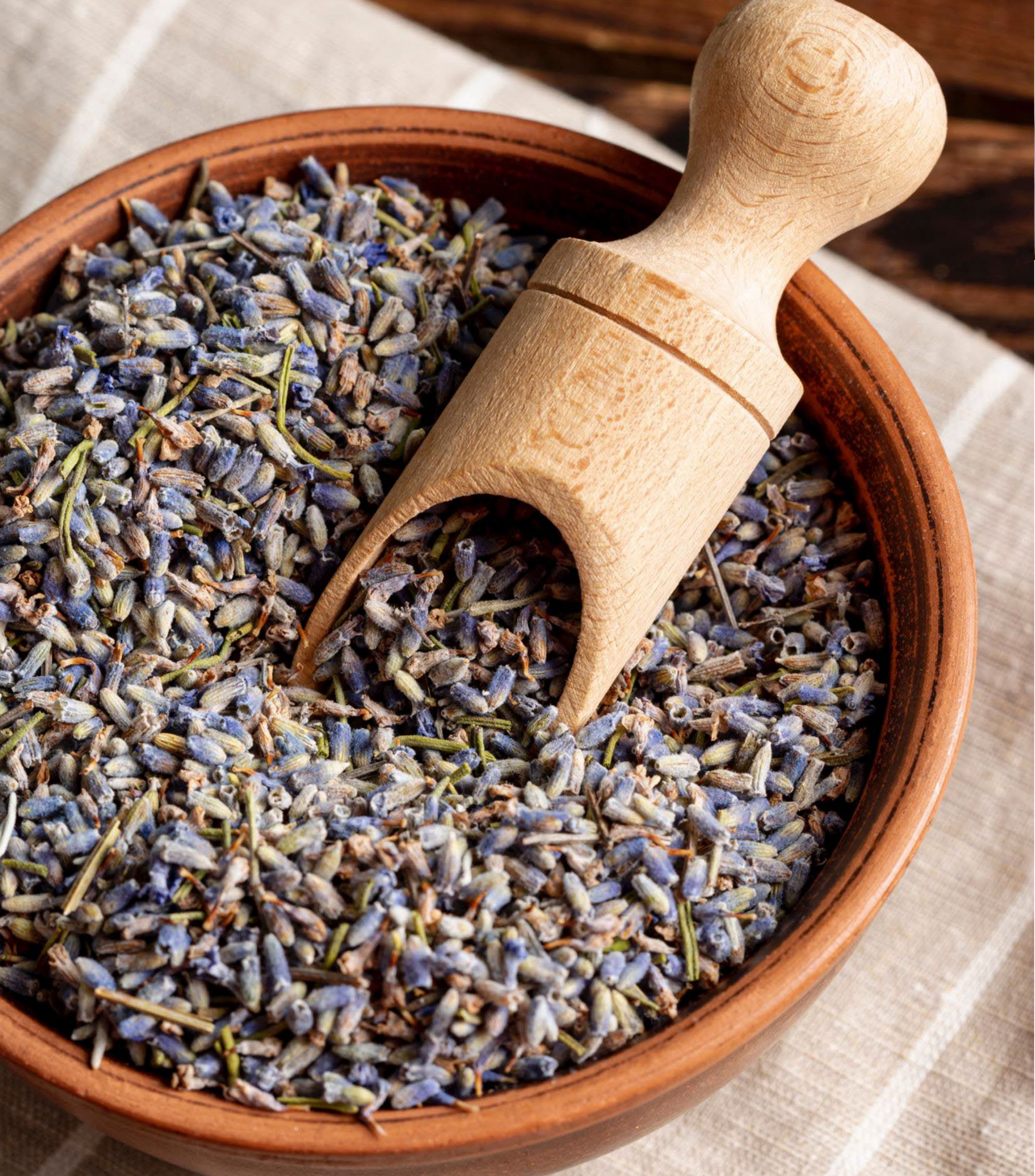 Dried lavender buds in a clay bowl with a wooden scoop