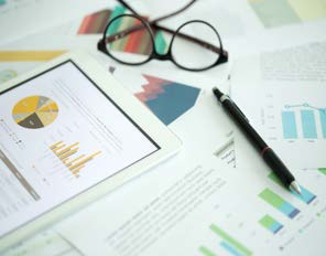 Tablet displaying financial charts with glasses and documents on desk