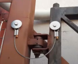 Close-up of a brown gate hinge with a safety cable loop for fall-over protection.