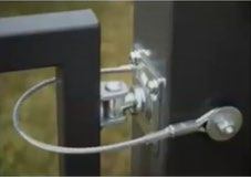 Detail of a silver gate hinge assembly featuring a steel safety cable attached to the post and gate frame.