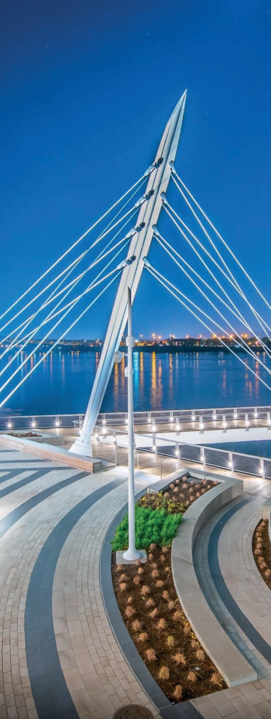 Illuminated cable-stayed pedestrian bridge and waterfront promenade at dusk