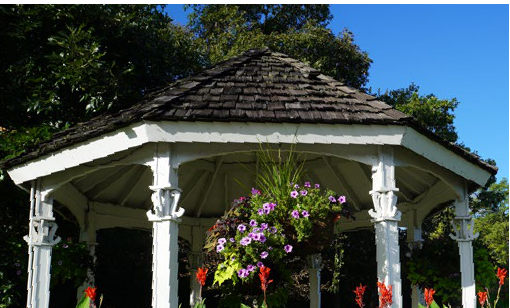 White wooden Victorian gazebo adorned with hanging flowering baskets at Smith Gardens
