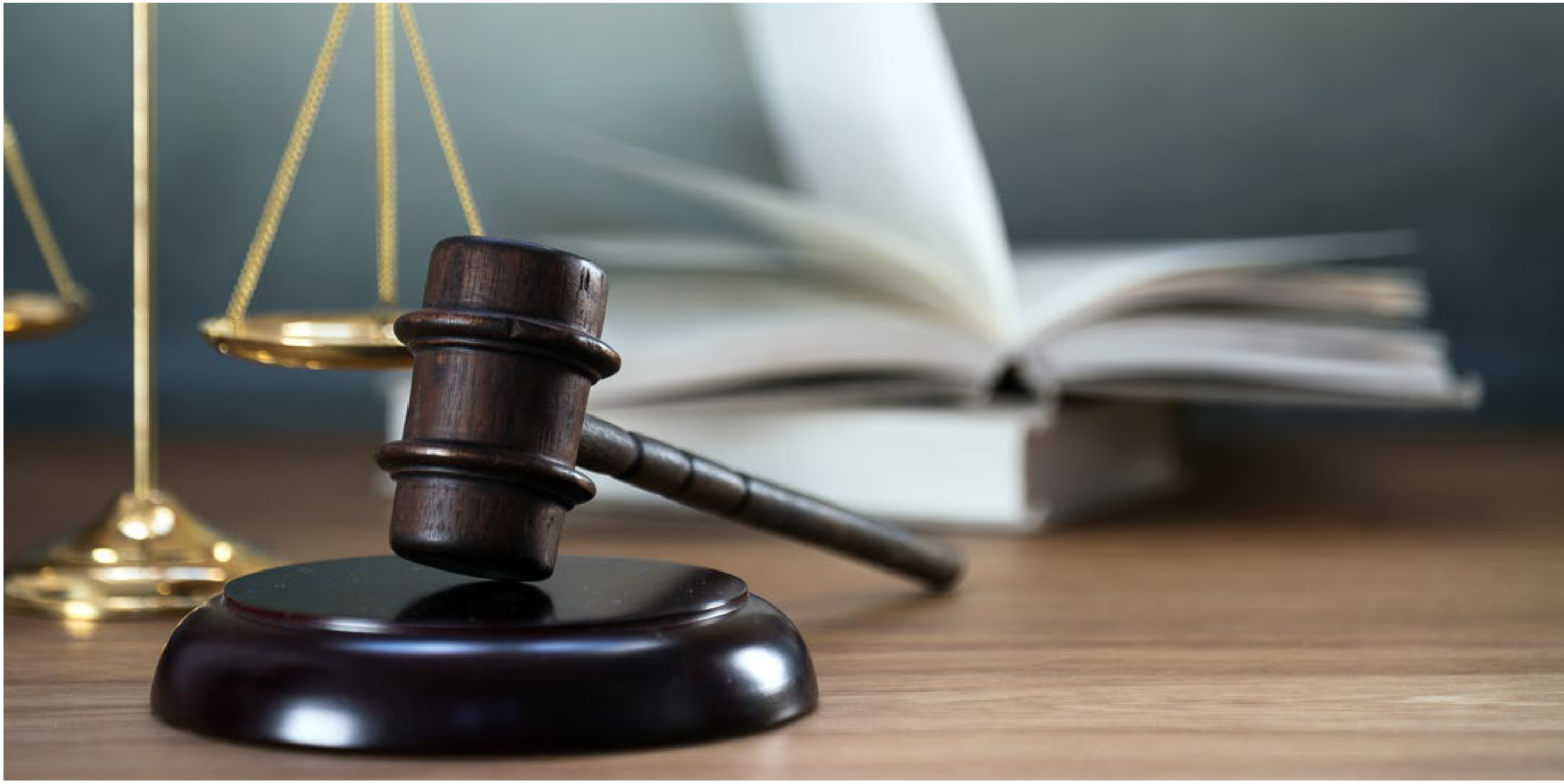 Wooden gavel resting on sound block with brass scales of justice and open law book on a desk
