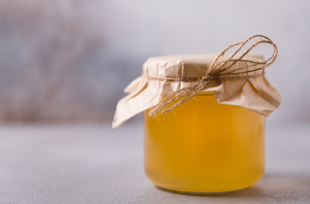 Glass jar with yellow contents and paper lid secured with twine