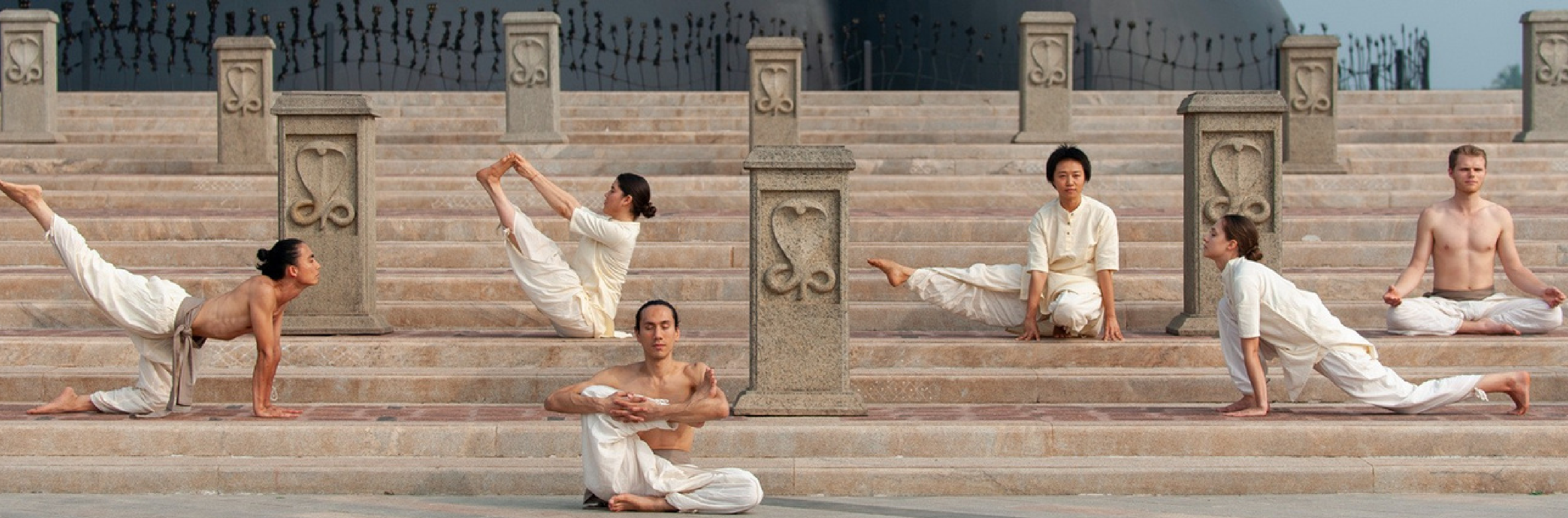 People performing advanced yoga asanas on large stone steps