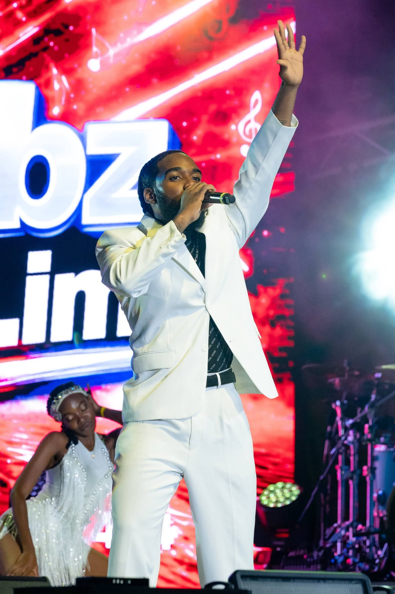 Jabz York performing live on stage in a white suit holding a microphone with a stage dancer in the background