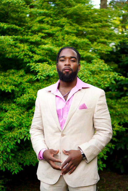 Jabz York in a beige linen suit with a pink shirt against lush green foliage