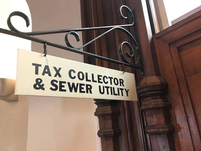 Tax Collector and Sewer Utility sign hanging from decorative wrought iron fixture