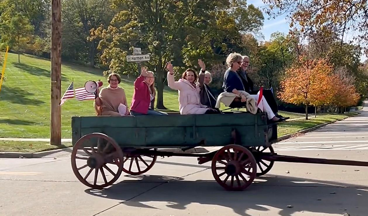People waving from a wagon on a residential street