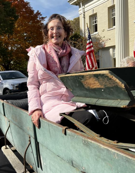 Woman wearing a pink coat smiling while seated in a green wagon
