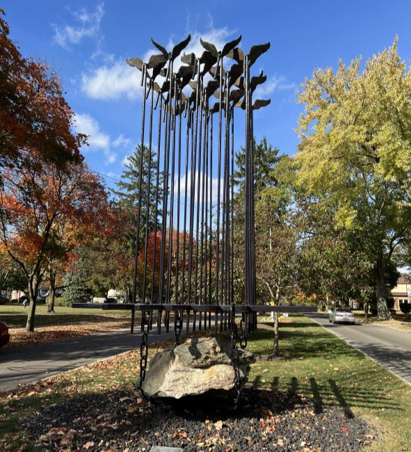 Tall outdoor metal sculpture of flying birds above a large rock
