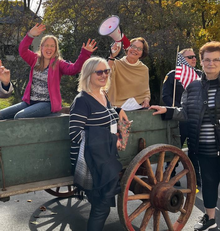 Group of cheerful people around a wagon wheel, woman holding a megaphone
