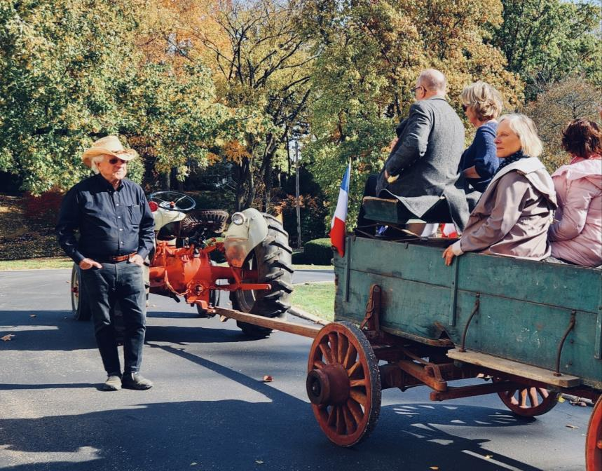 Man in cowboy hat standing next to a tractor hitched to a wagon full of people