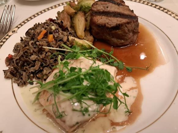 Plated dinner course featuring steak, salmon, and wild rice