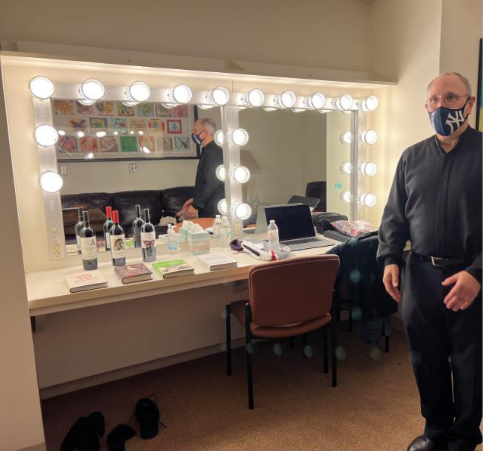 Backstage vanity mirror setup in dressing room with masked individual standing