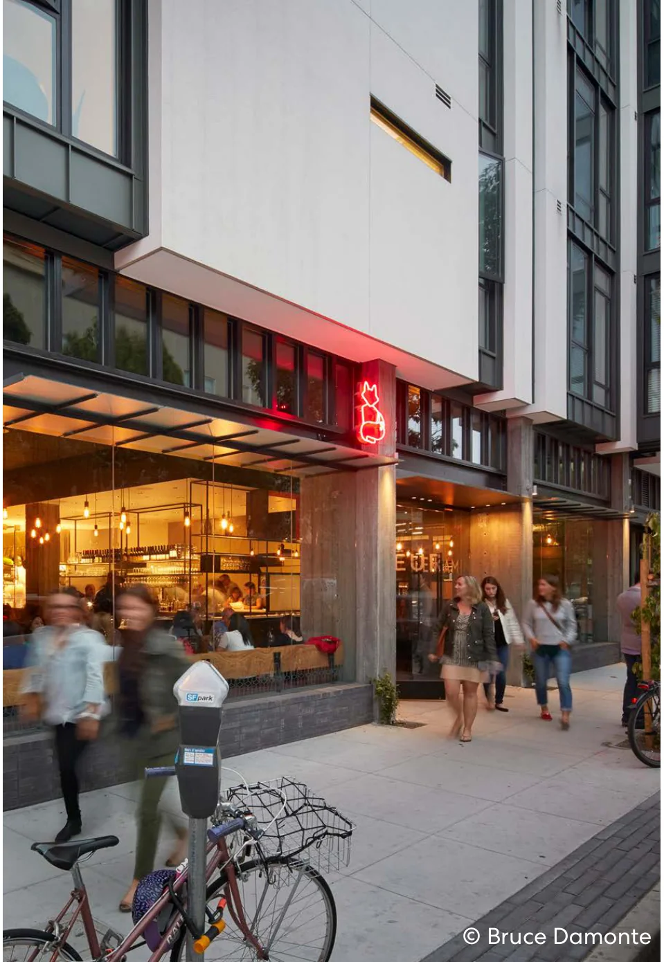 Pedestrians walking past an active ground floor restaurant with warm lighting and indoor-outdoor frontage