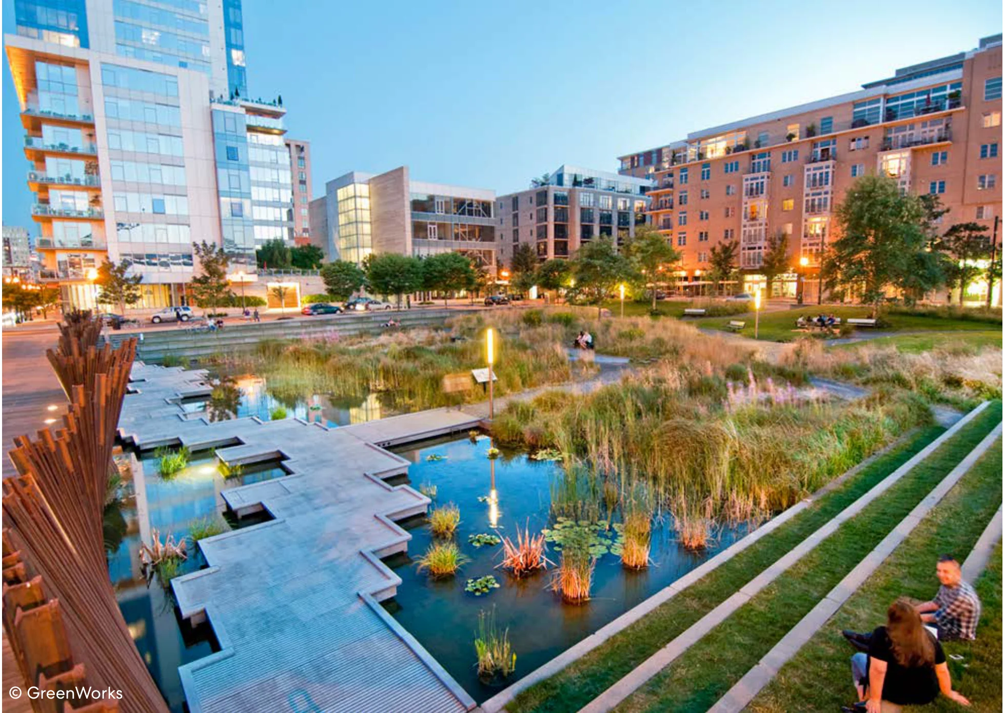 Tanner Springs Park in Portland featuring an urban wetland with boardwalks, native reeds, terraced seating, and adjacent residential and commercial buildings at dusk.