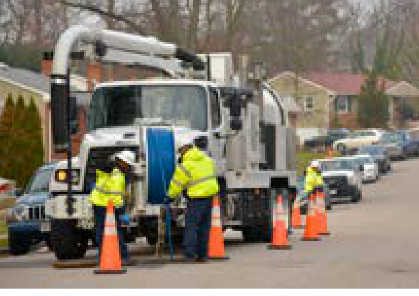 Utility trucks and workers maintaining water and wastewater infrastructure on a residential street