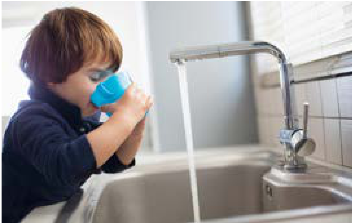 Young child drinking fresh water from a blue cup near a sink