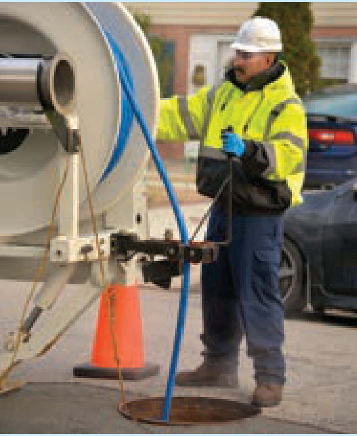 Utility technician operating wastewater maintenance equipment at a street manhole