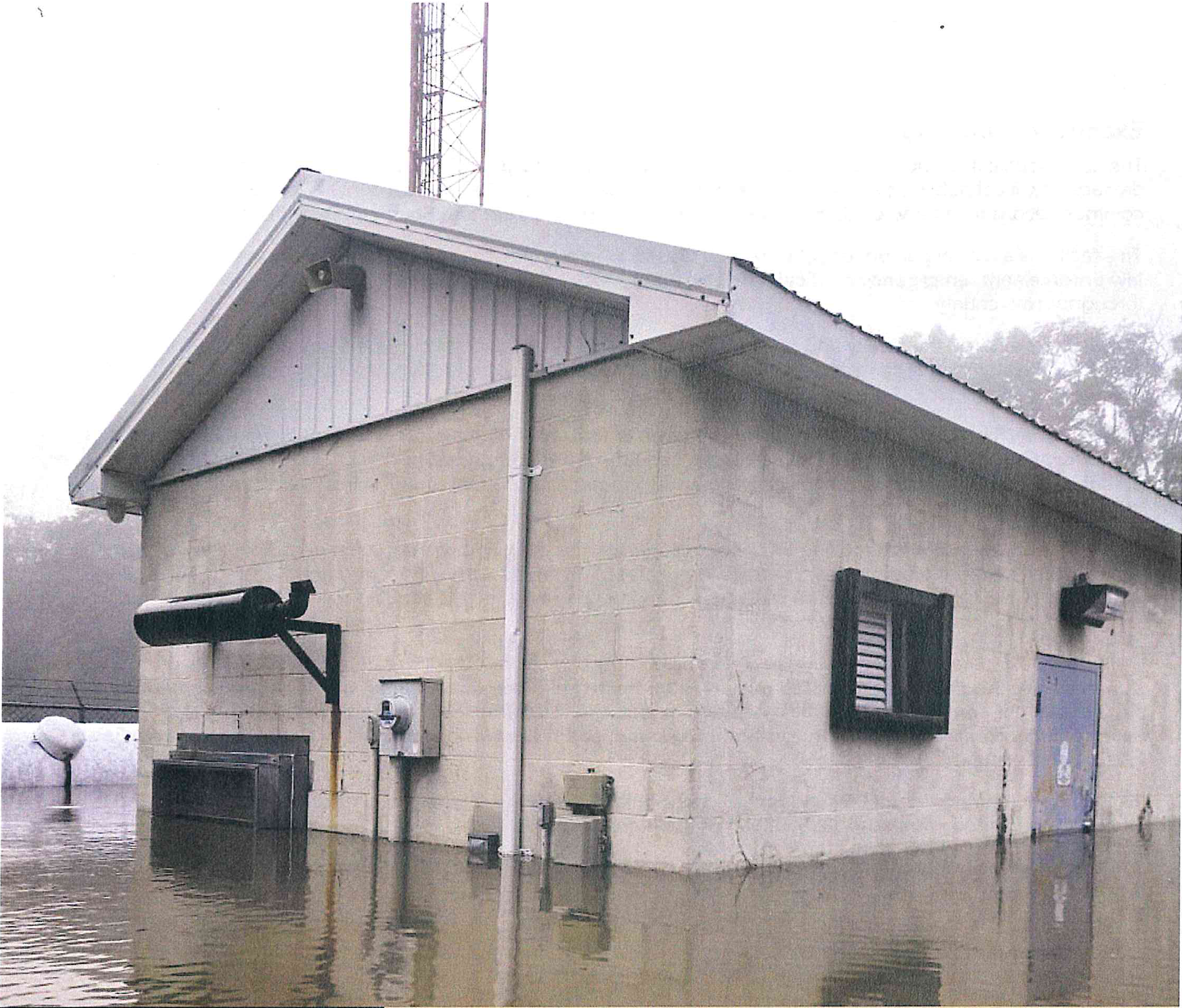 Flooded Sampson Avenue Public Safety Communications Facility building surrounded by standing water with communications tower behind
