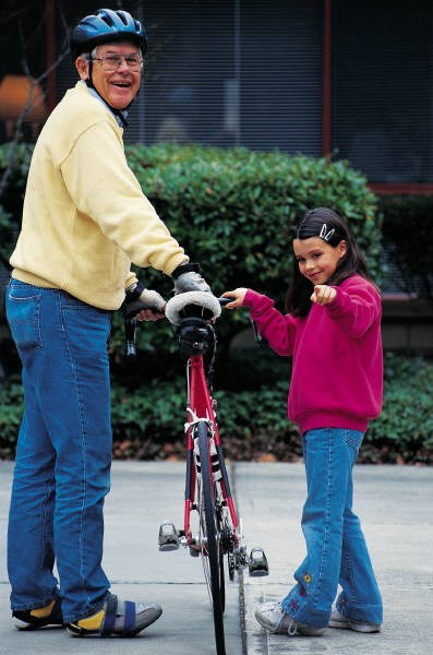 An adult cyclist in helmet with bicycle smiling alongside a happy young girl