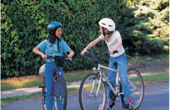 Two young girls wearing bike helmets pausing and chatting on their bicycles outdoors