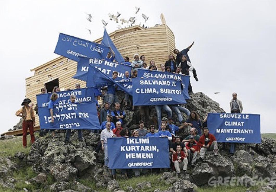 Activistas de Greenpeace posando con pancartas frente a una réplica de madera del Arca de Noé en una ladera rocosa.