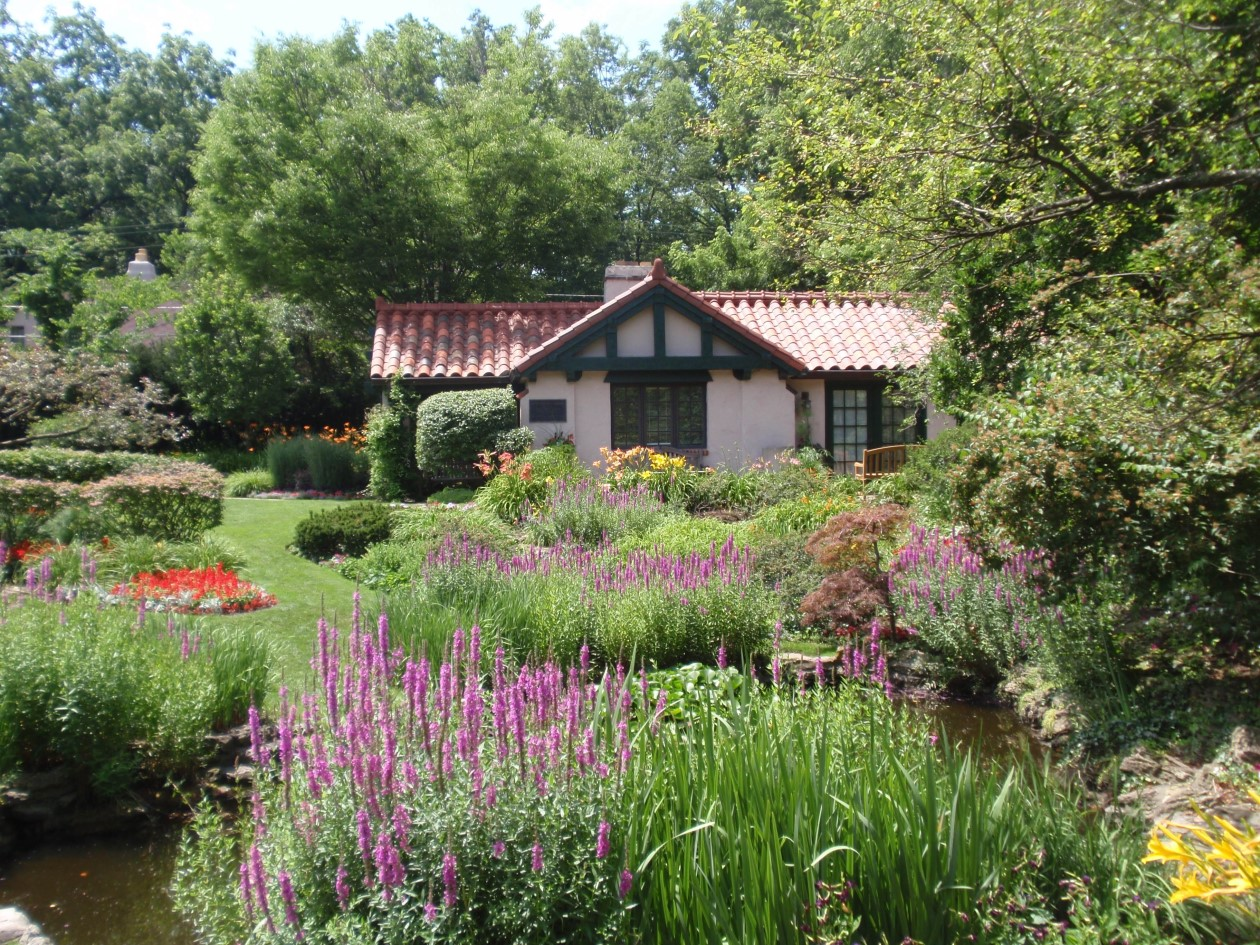Lush, blooming floral garden surrounding the historic cottage at Smith Gardens with pond in the foreground