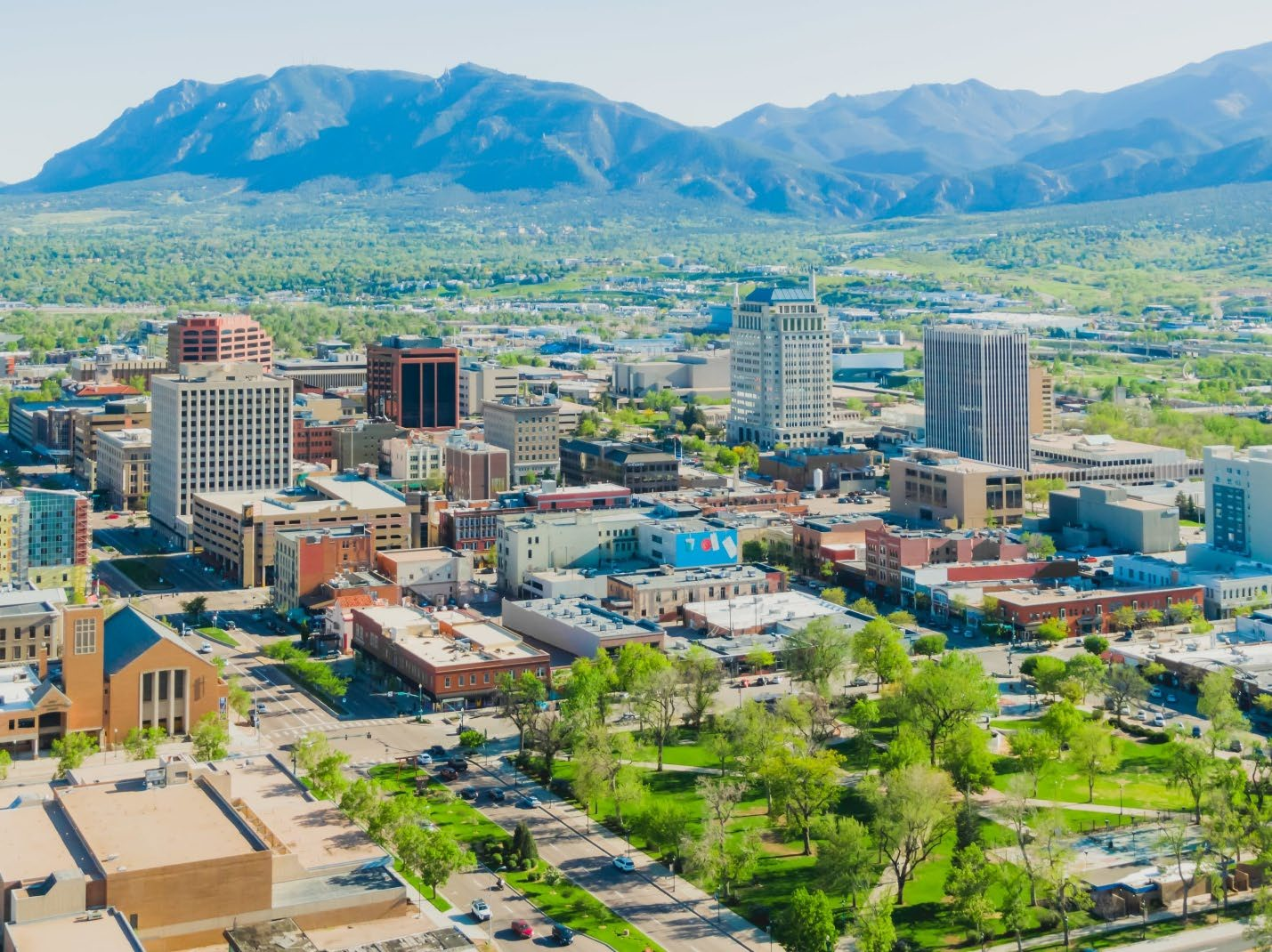 Aerial landscape view overlooking downtown Colorado Springs with trees and urban architecture set against the Rocky Mountains