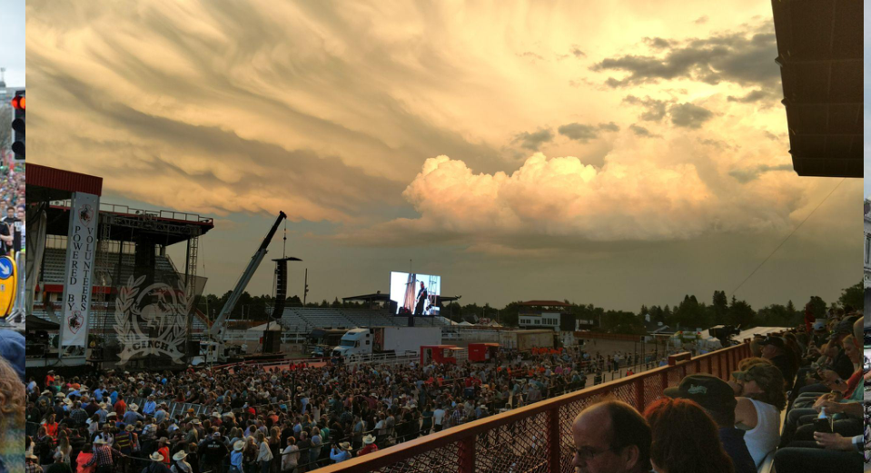 Large crowd at an outdoor stage under a dramatic sunset sky